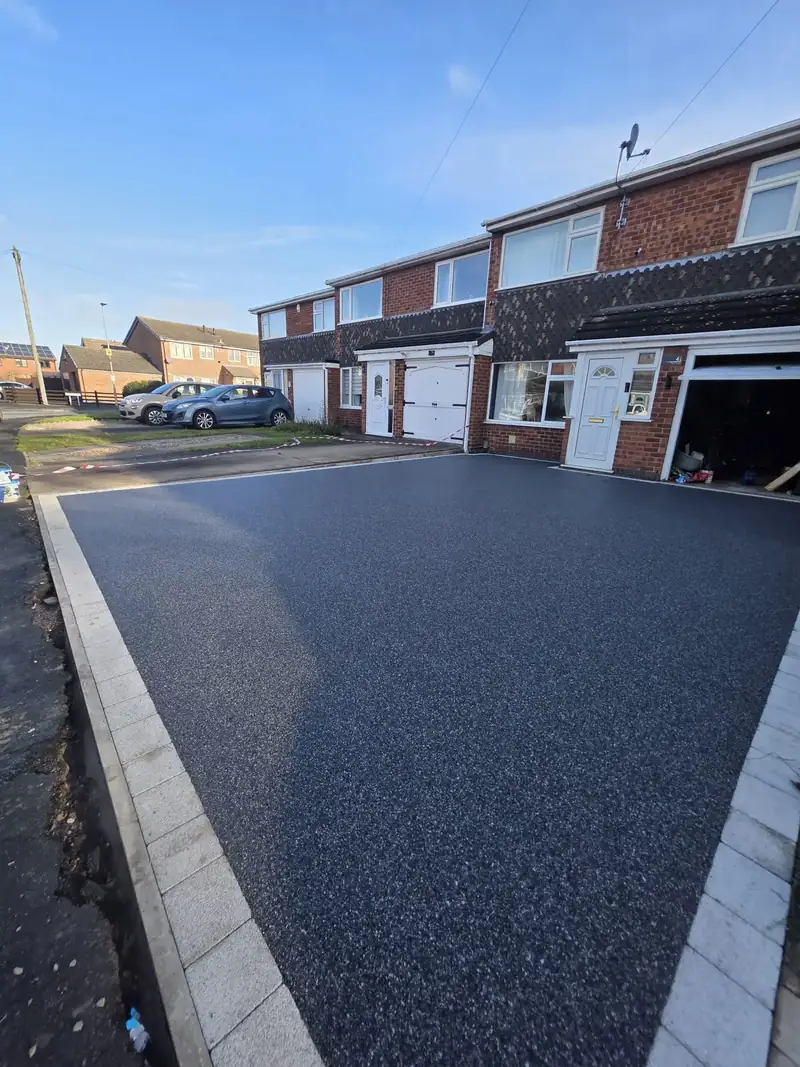Dark charcoal resin driveway with a pale block paved border alongside a semi-detached house