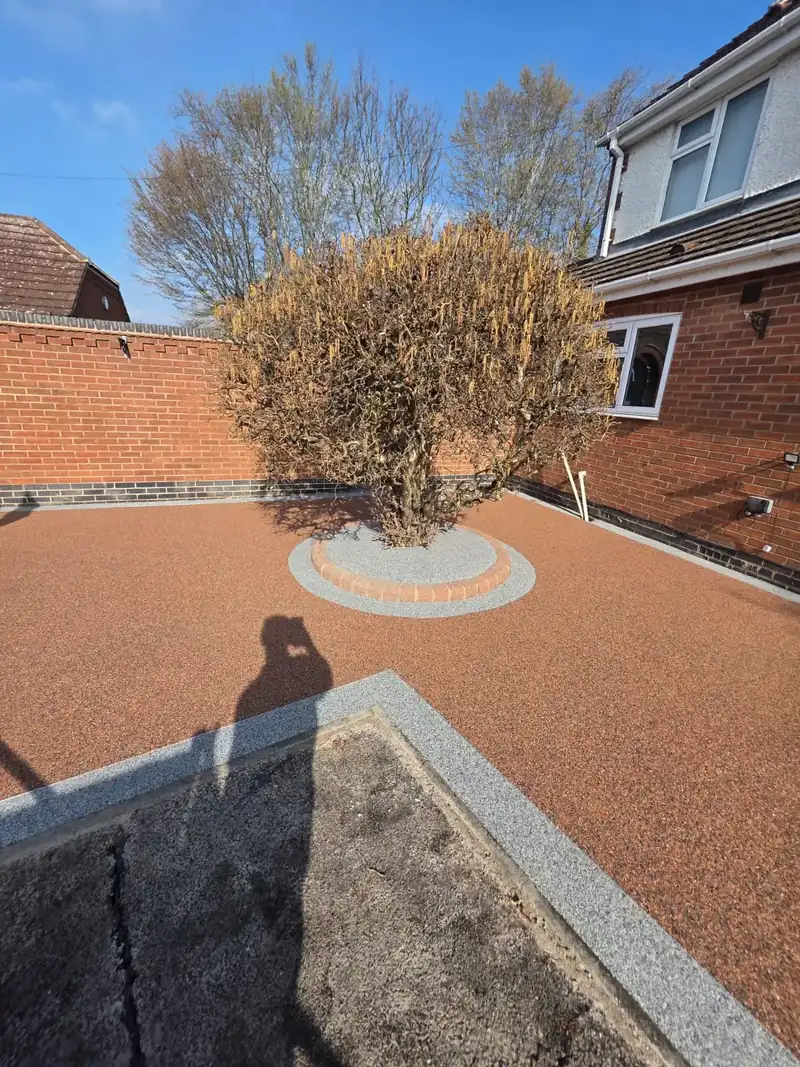 Copper-toned resin driveway with a circular planted feature set into the surface