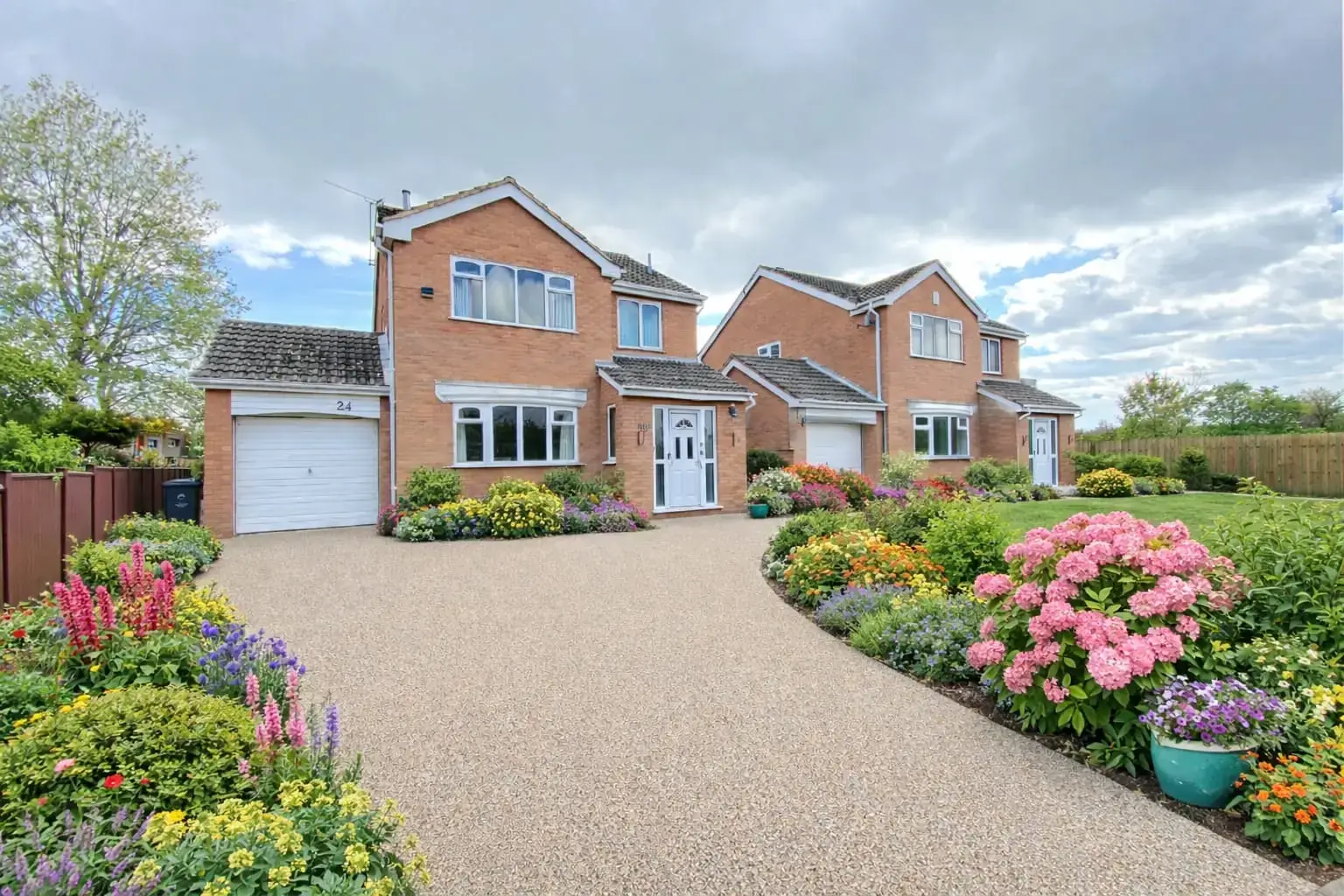Gold resin bound driveway leading to a detached house with planted borders